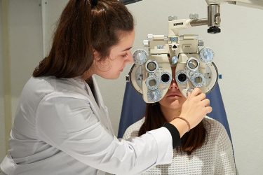 Óptico-optometrista trabajando en el gabinete con un paciente.