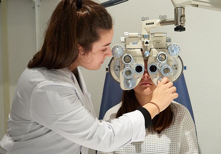 Óptico-optometrista trabajando en el gabinete con un paciente.